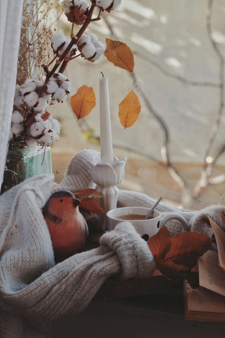 A collection of cozy bird-themed gifts for fall, including a bird mug, knitted scarf, and autumn leaves